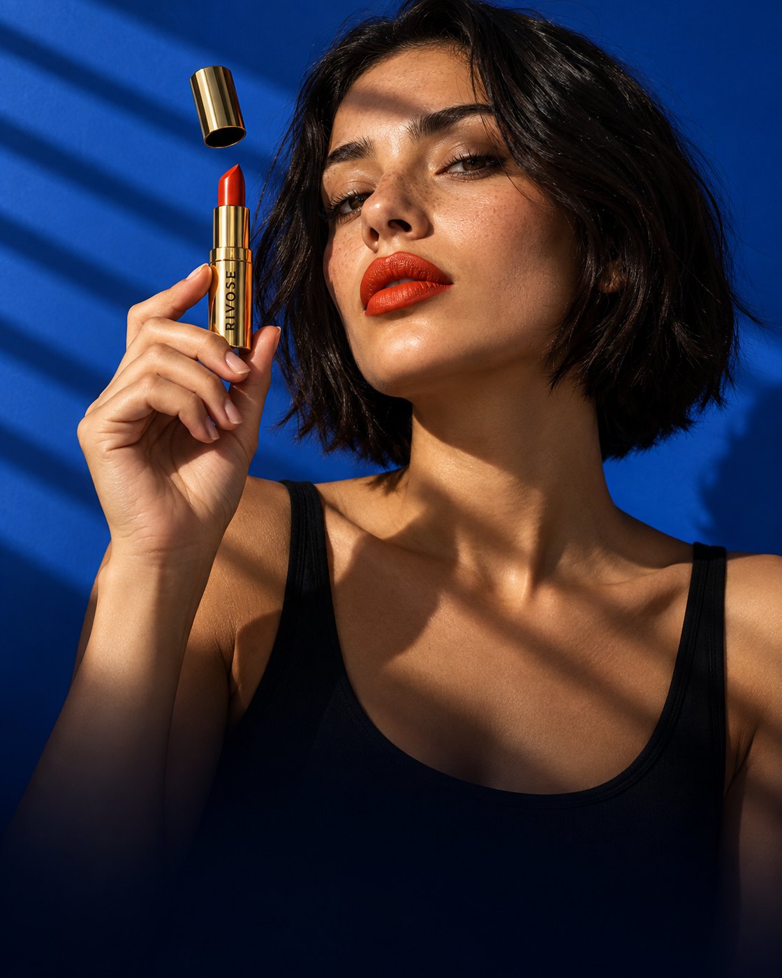 A woman holds up a red lipstick in a gold case, blue background