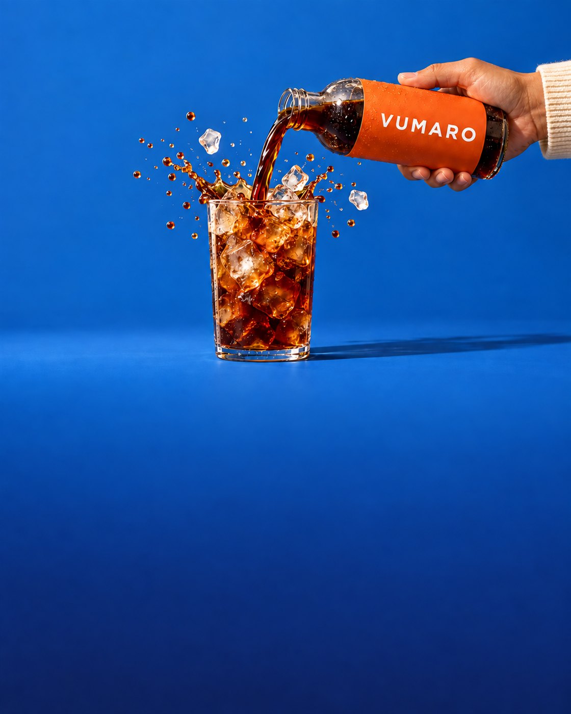 Cold brew poured from an orange bottle into a glass of ice, splash frozen, blue background